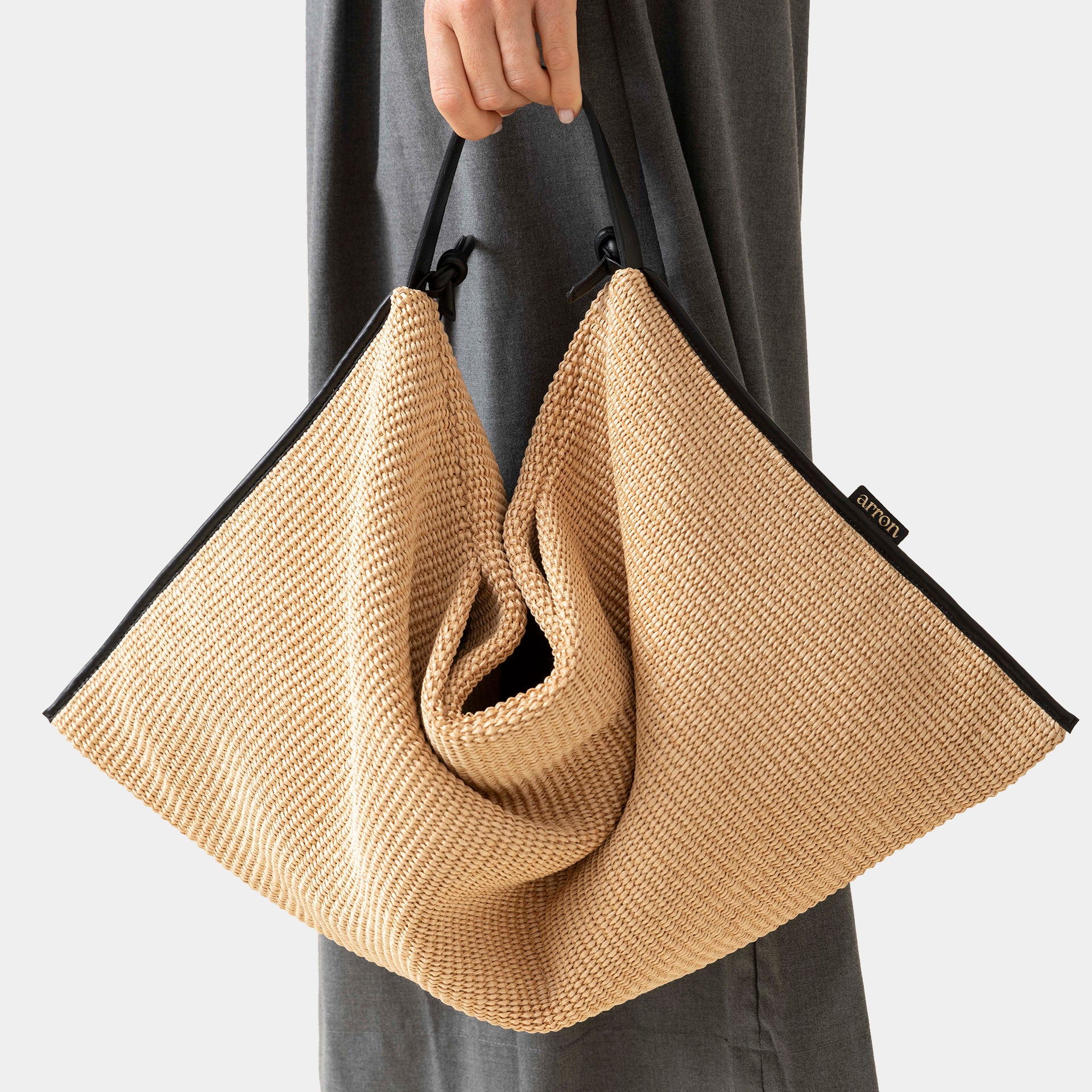 borsa Futura del brand Arron in rafia ecrù con bordi in pelle nera destrutturata dettaglio portata a mano