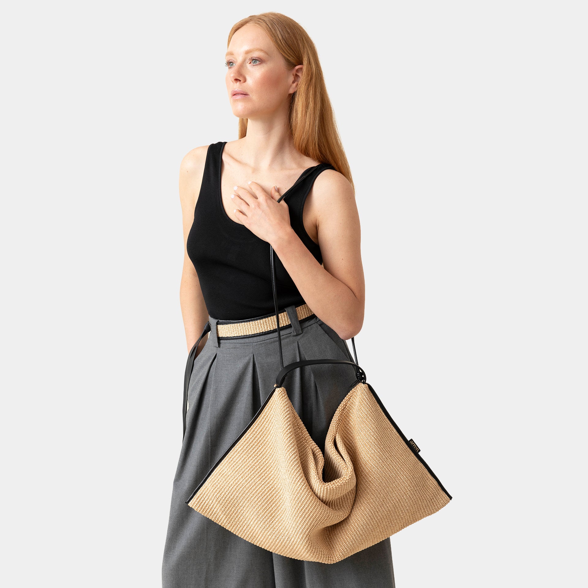 borsa Futura del brand Arron in rafia ecrù con bordi in pelle nera destrutturata con tracolla indossata a spalla